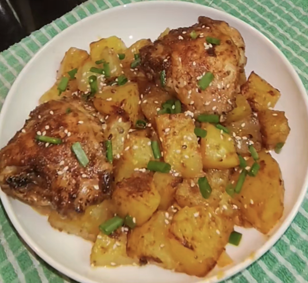 Air fryer chicken thighs and potatoes on a white plate, topped with green onions and sesame seeds