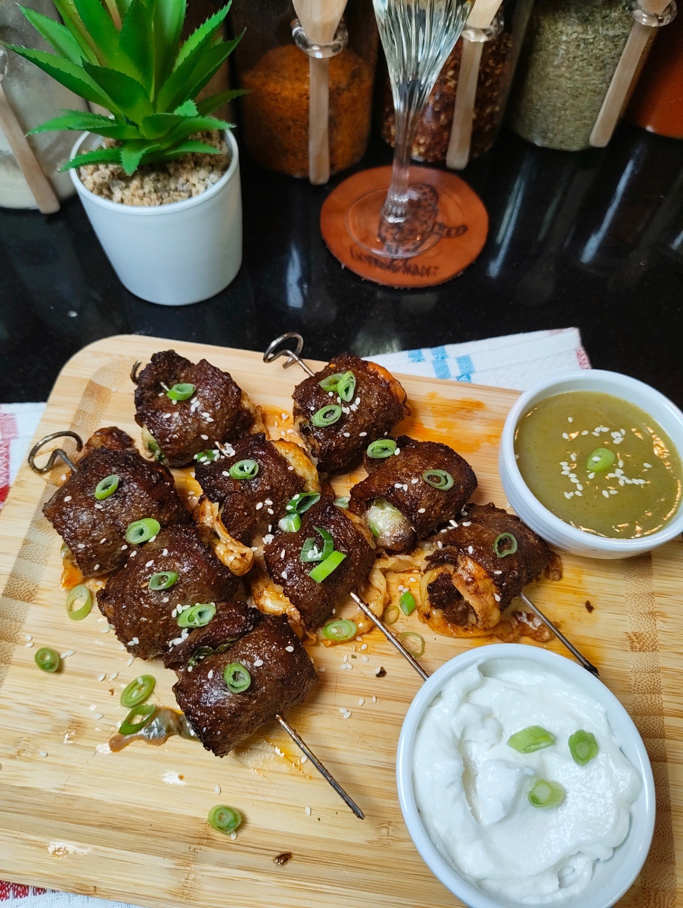 Spinach and mozzarella stuffed beef skewers on a wooden board served with garlic sauce and green chilli sauce