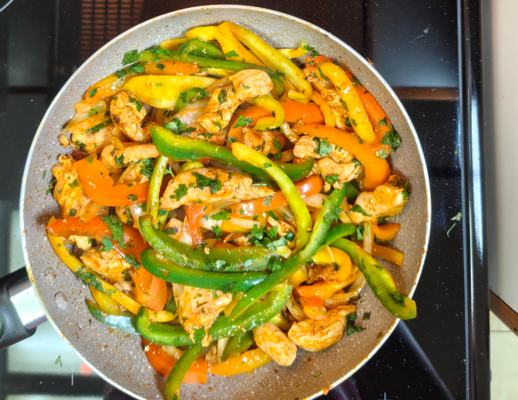 Cooked chicken with colourful bell pepper strips in a pan