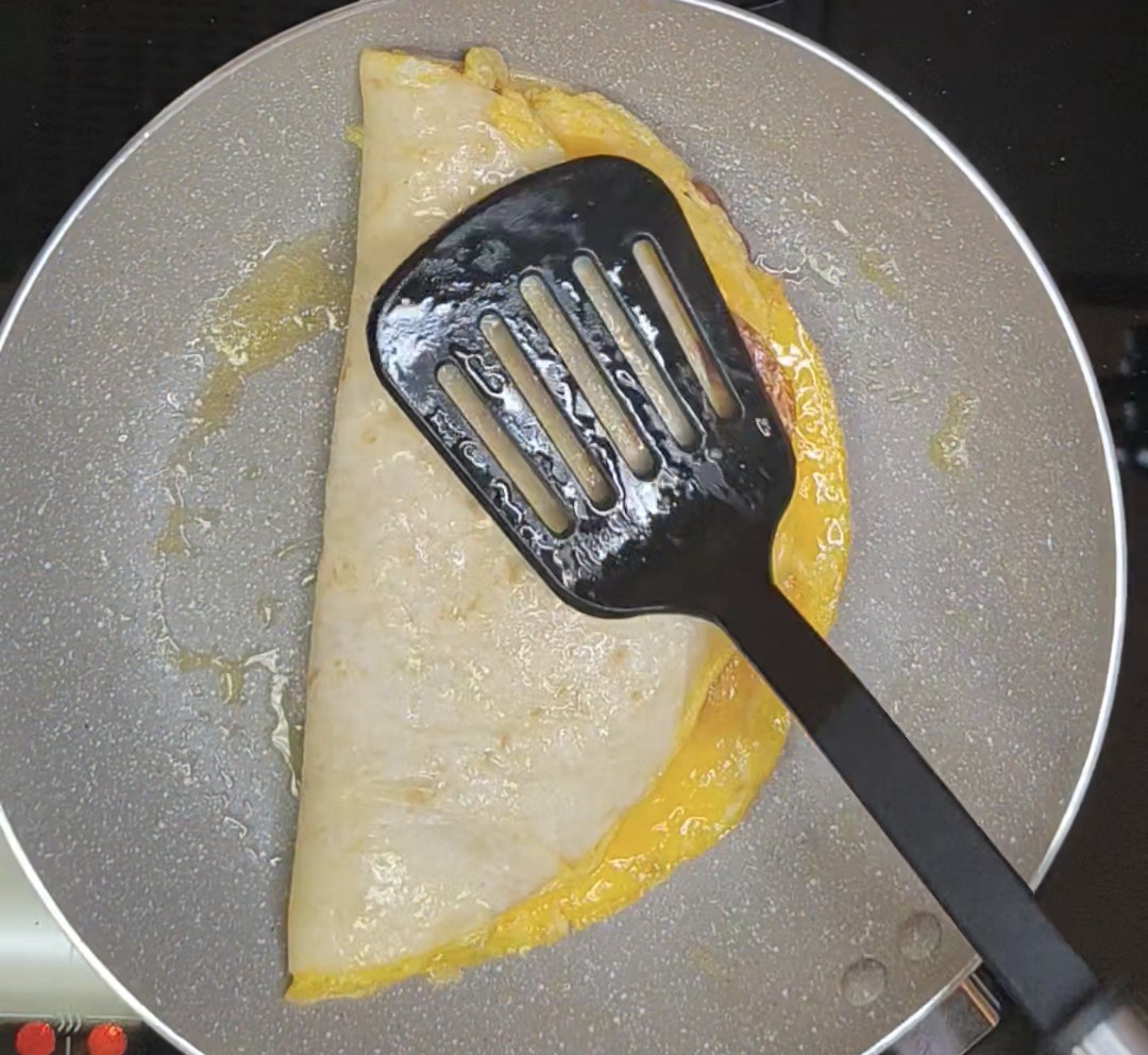 Egg, salami and cheese tortilla folded in half in a frying pan