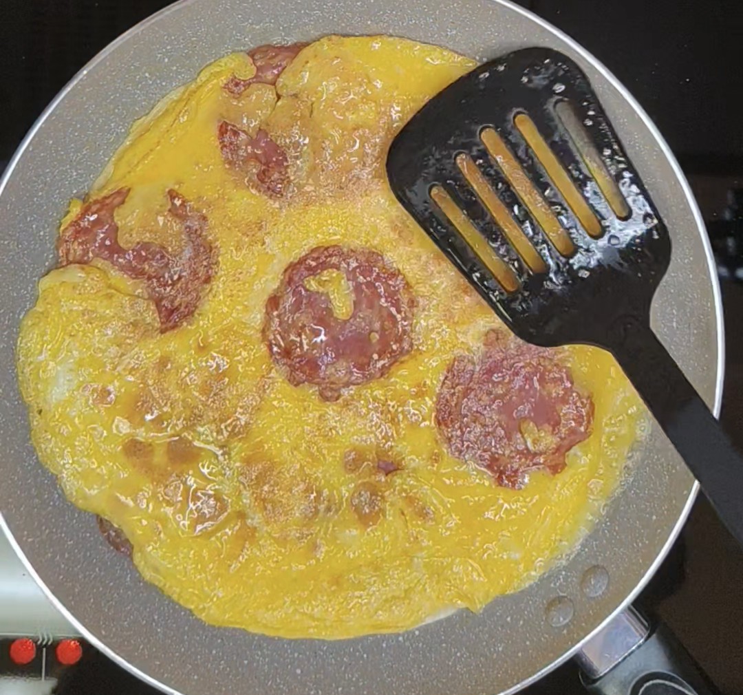 Cooked egg and salami layer being turned in a frying pan
