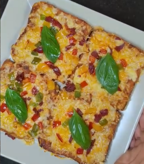 Four cheesy air fryer bread pizzas topped with peppers, red onion and fresh basil on a white plate