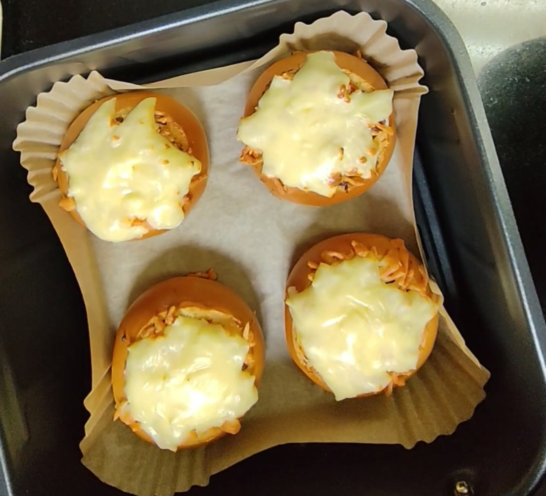 Four stuffed brioche buns with melted mozzarella in a lined air fryer basket after cooking