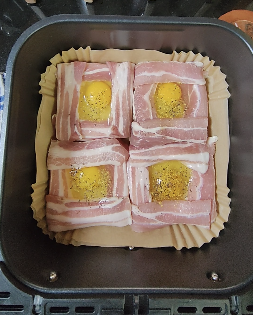 Four bacon and egg portions arranged on a parchment-style liner in an air fryer basket