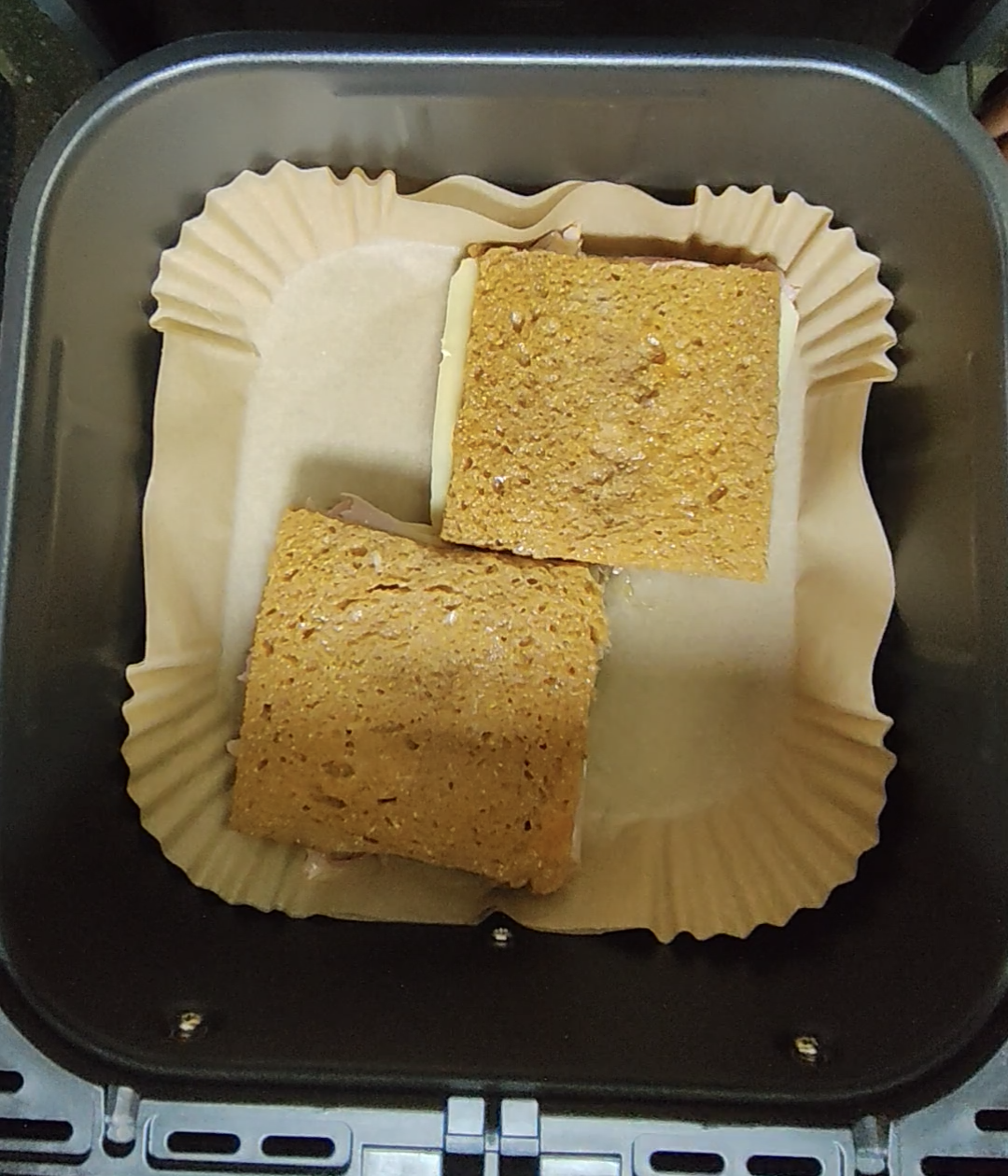 Two sandwiches arranged on a parchment-style liner in an air fryer basket