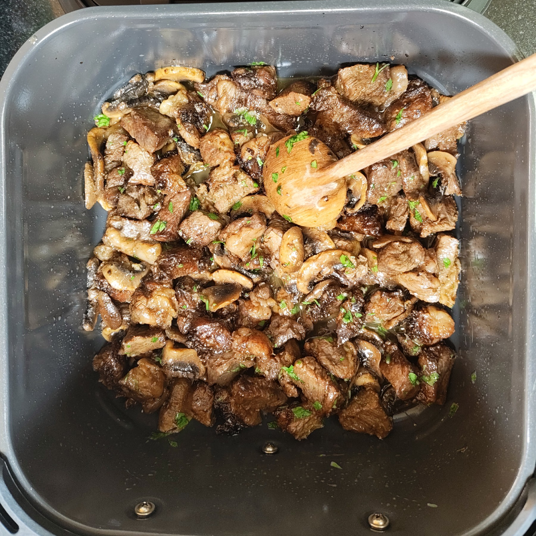 Finished beef and mushrooms mixed with melted parsley garlic butter in the air fryer basket