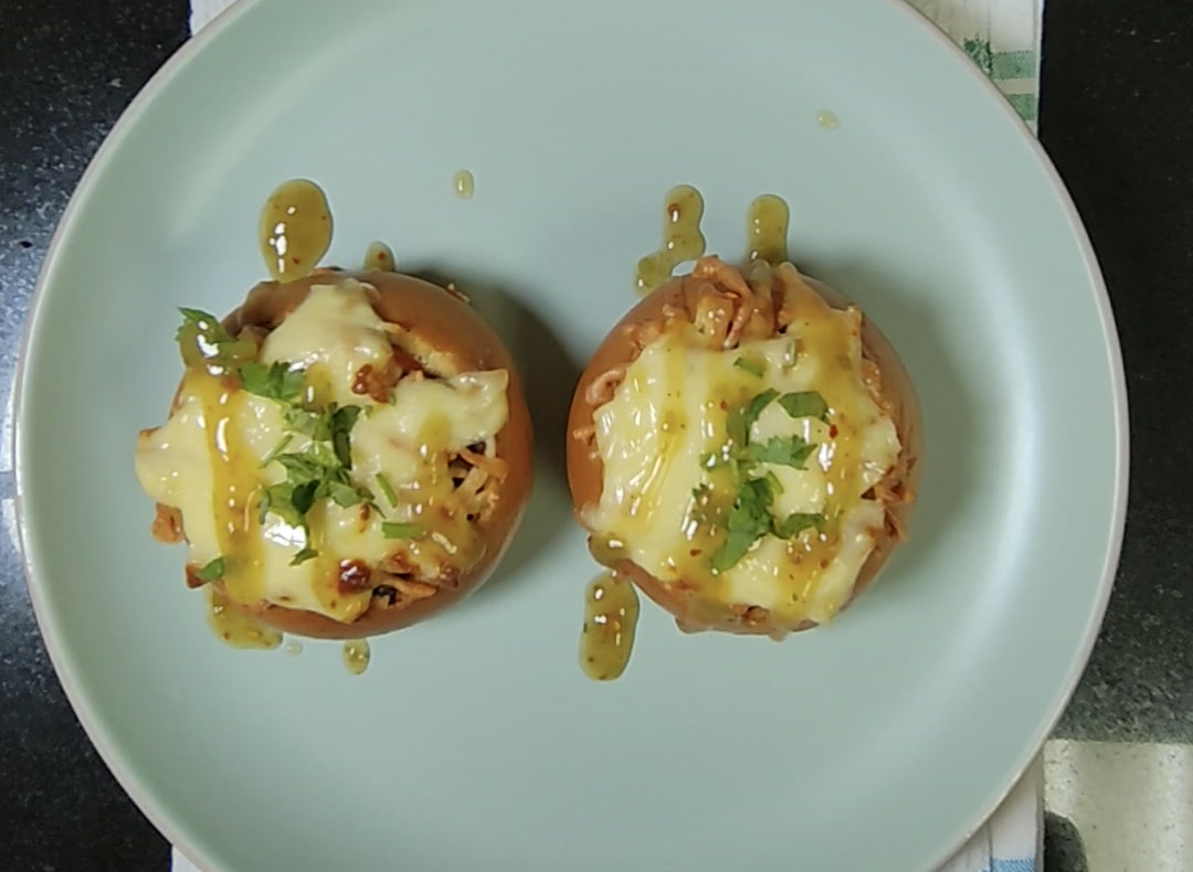 Two stuffed brioche buns on a pale green plate, topped with melted mozzarella, fresh coriander and a drizzle of green chilli sauce