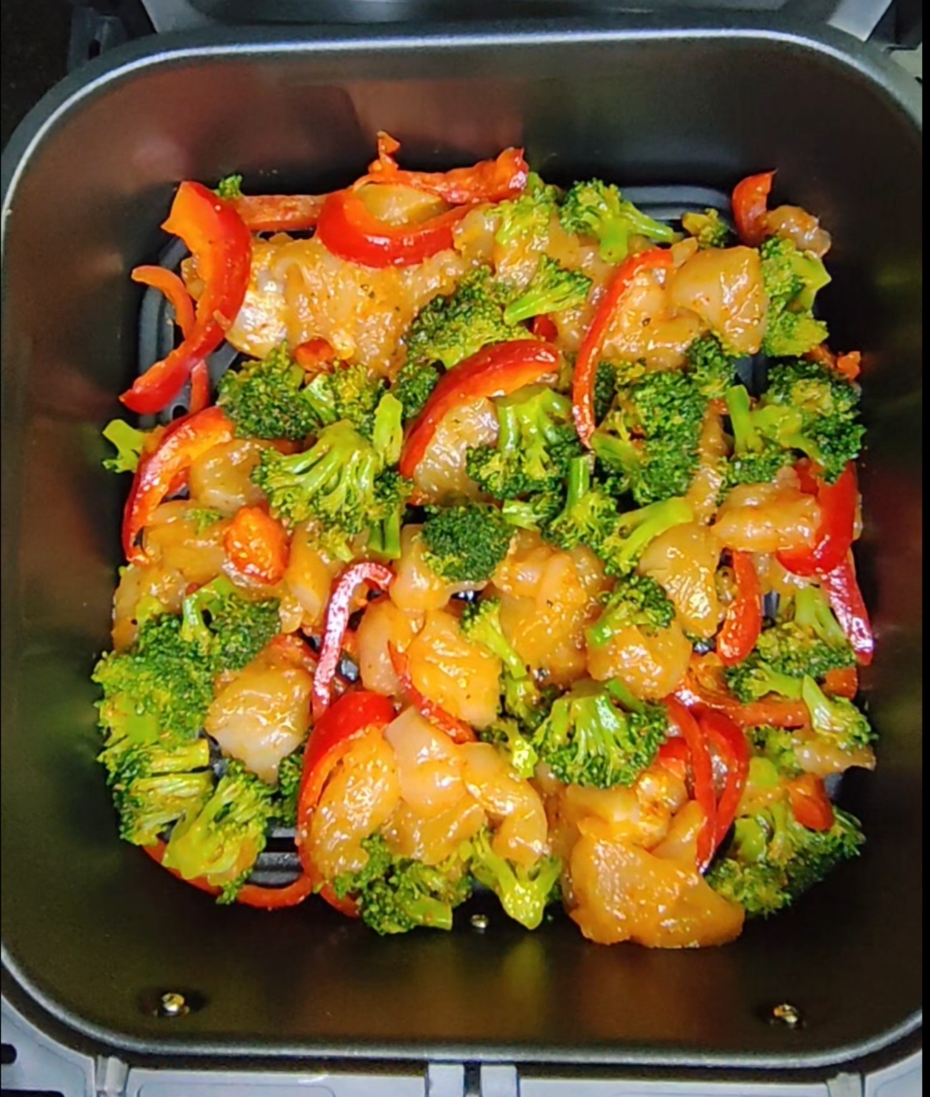 Broccoli and red pepper in an air fryer basket as part of a mixed meal