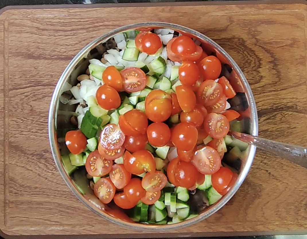 Cooked black eyed peas with chopped cucumber, white onion and halved cherry tomatoes being assembled in a metal bowl