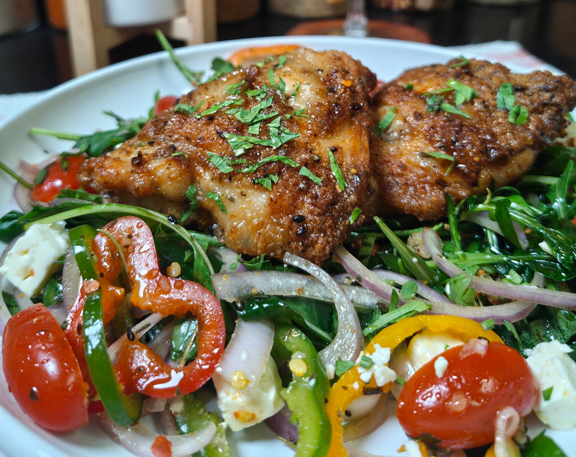 Crispy air fryer chicken thighs topped with fresh parsley, served on a colourful rocca salad