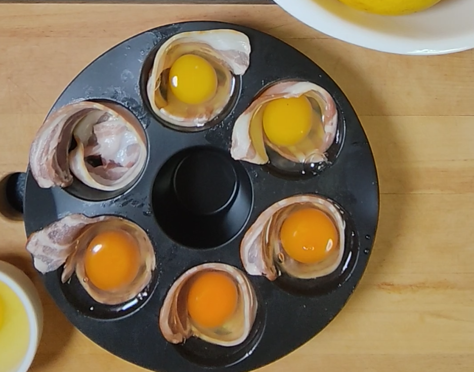 Raw eggs cracked into a bacon lined silicone mould on a wooden board