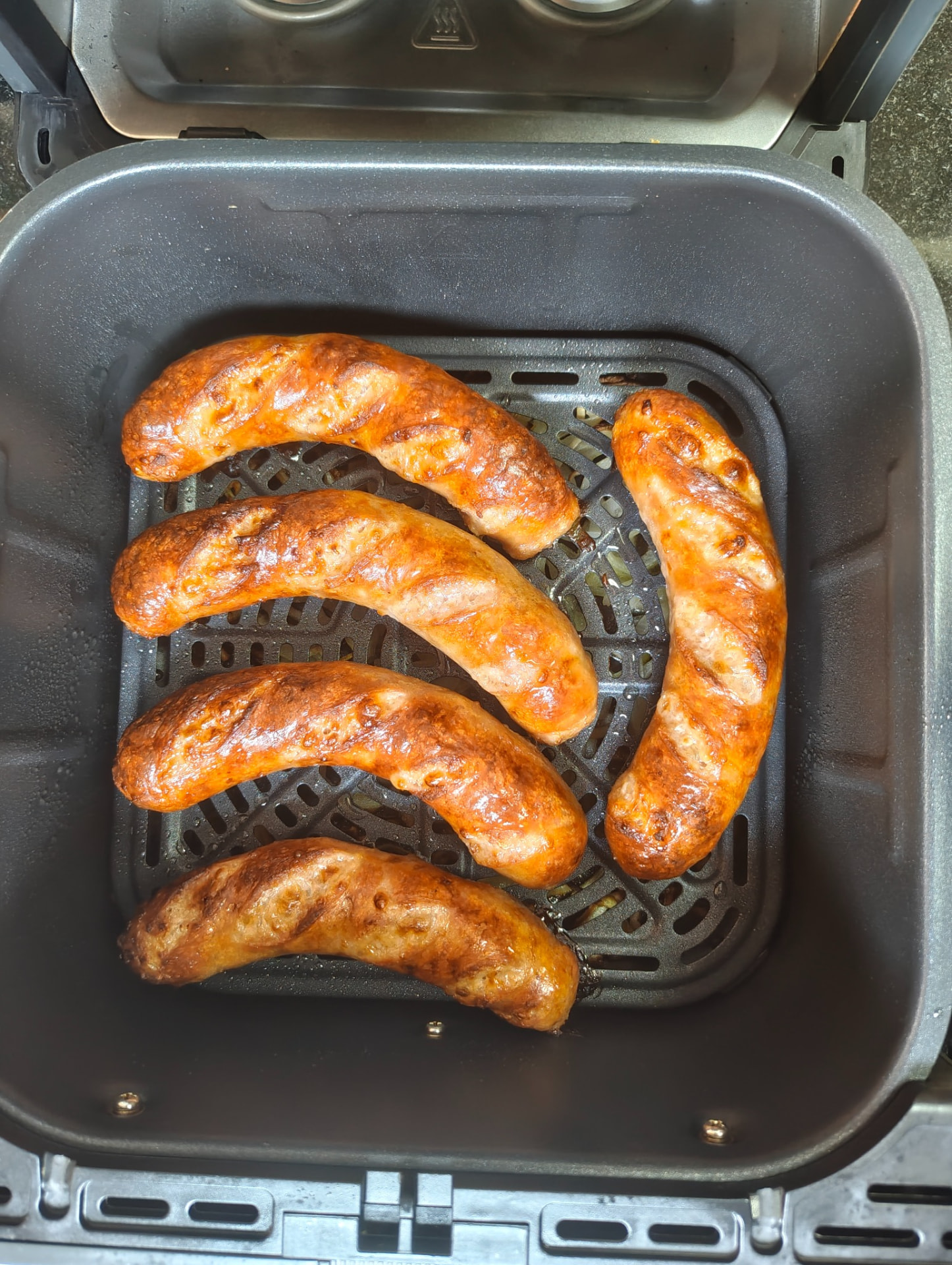 Cooked chicken sausages browned in an air fryer basket